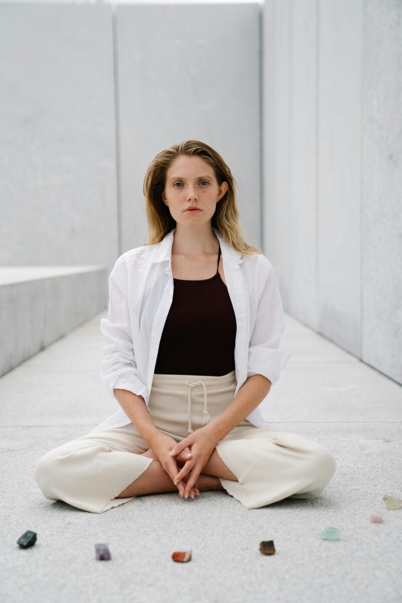 Los 10 cristales más poderosos para la meditación 13 Serene woman meditating on a white floor with colorful gemstones around her in a minimalist setting.